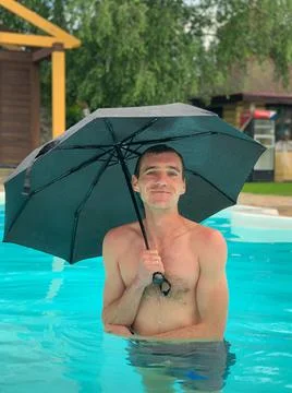 Attractive smiling man in the pool under umbrella at sunny day Foto stock