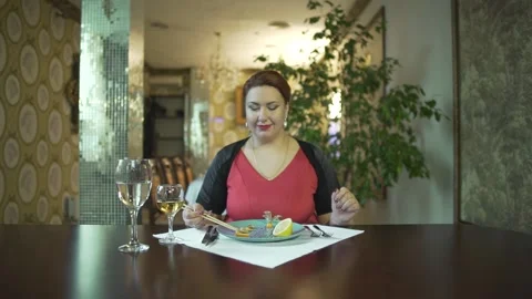 Attractive smiling middle aged brunet woman in red dress eating food with chopst Stock Footage 137537333