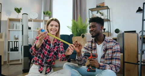 Attractive smiling modern multiracial couple sitting together on the floor in Stock Footage 158562938