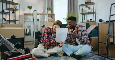 Attractive smiling modern young multiracial couple sitting on the floor in new Stock Footage 158558956