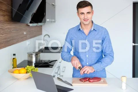 Attractive Smiling Young Man Cooking Meat On The Kitchen