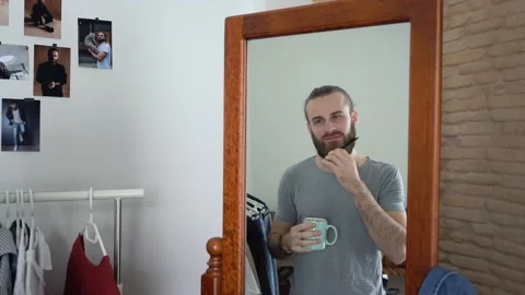 Attractive Stylish man is Combing His Beard Drinking  coffee looking at a mirror Stock Footage 147894194