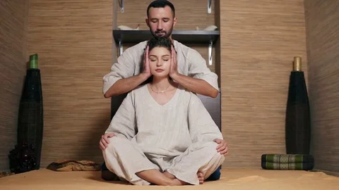 Attractive thai massagist is massaging young woman's head sitting behind her Stock Footage