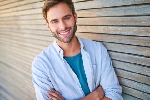Attractive white guy smiling at camera leaning against wooden cladding Stock Photos