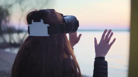 Attractive white woman is using virtual reality glasses by the lake at sunset Stock Footage 74739276