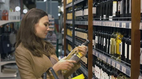 Attractive woman chooses the wine bottle at the supermarket Stock Footage