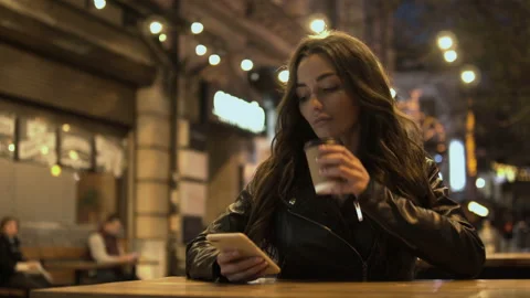 Attractive woman drinking coffee using a mobile phone while walking through the Stock Footage 98033124