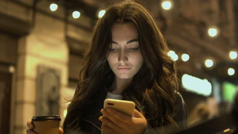 Attractive woman drinking coffee using a mobile phone while walking through the Stock Footage 98040845