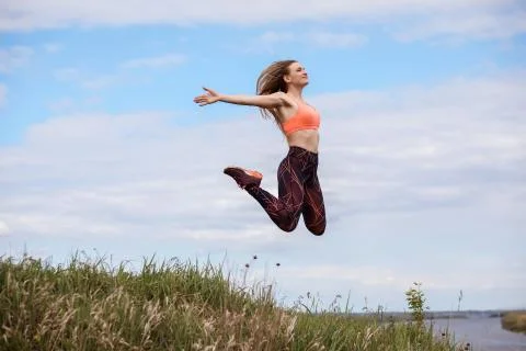 Attractive woman is jumping in the air, doing fitness exercises outdoors. Stock Photos