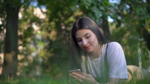 Attractive woman lies on grass in park and use mobile phone, relax summer Stock Footage