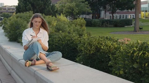 Attractive woman making notes in notebook sitting outdoor alone closeup. 動画素材 289399055