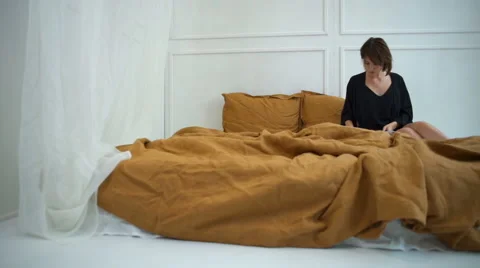 Attractive woman in silk home dress reading a magazine in bed Stock Footage