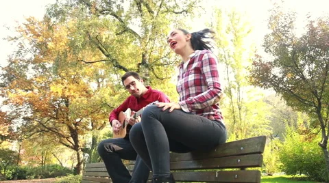 Attractive woman singing while man playing guitar in park Stock Footage 59557010
