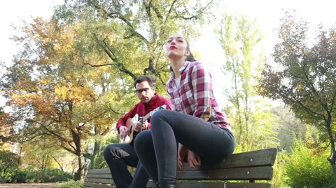 Attractive woman singing while man playing guitar in park Stock Footage 59557015