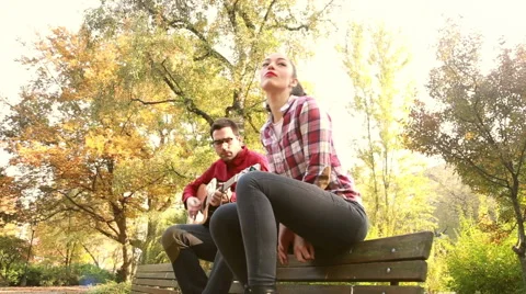 Attractive woman singing while man playing guitar in park Stock Footage 59557016