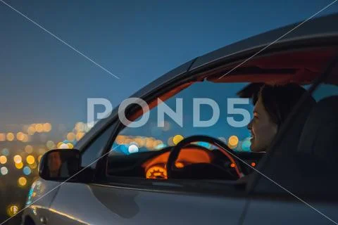 The attractive woman sit in the car on the background of the city. night time Stock Photos