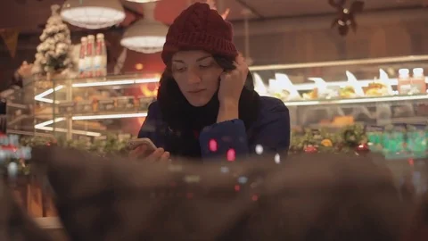 Attractive woman sitting in cafe using smartphone. New year's decorations Stock Footage 83080428