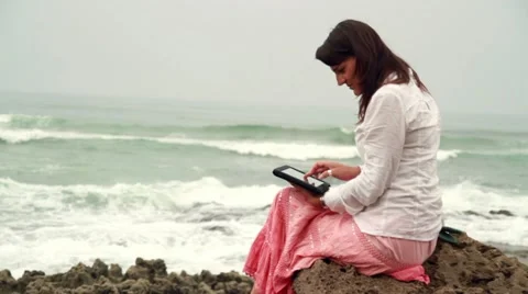 Attractive woman working on tablet computer on rocks at the sea Vídeos de archivo 10848563
