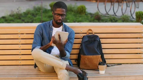 Attractive young african man in glasses using tablet for chatting with friend Stock Footage