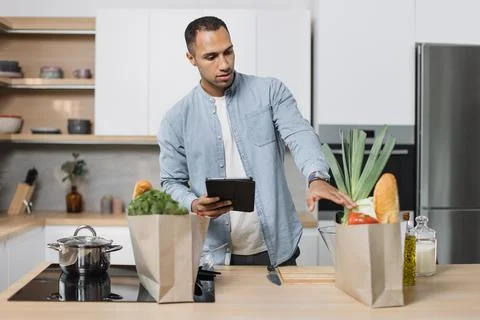 Attractive young arab man looking at an online recipe on a digital tablet. Stock Photos
