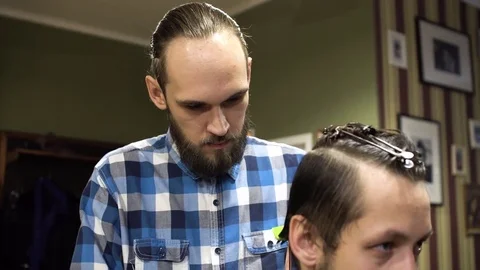 Attractive young barber is cutting human hair with the scissors. He is looking Stock Footage 69962935