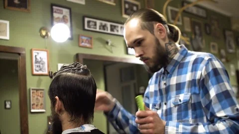 Attractive young barber is cutting human hair with the scissors. He is looking Stock Footage 69963173