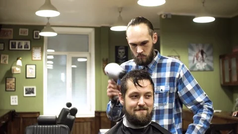 Attractive young barber is cutting human hair with the scissors. He is looking Stock Footage 69965190