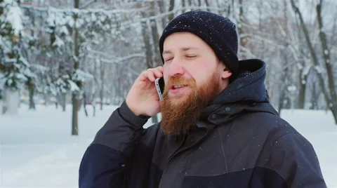 Attractive young bearded man talking on the phone. It goes in the winter park Stock Footage 65890533
