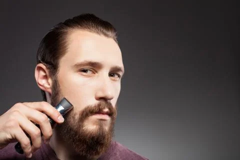 Attractive young bearded man is using shaver Stock Photos