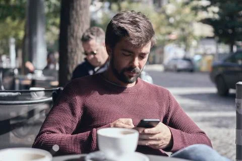 Attractive young bearded man using his smartphone in the cafe Stock Photos