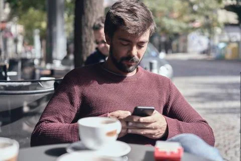 Attractive young bearded man using his smartphone in the cafe Foto stock