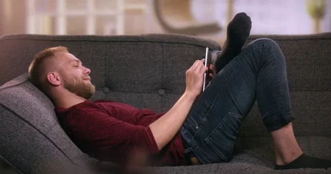 Attractive young boy lying on sofa using tablet Stock Footage 77191371