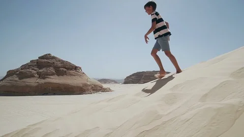 Attractive young boy running down by sand dune with rock in desert slow motion Stock Footage 108280556