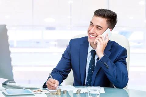 Attractive young businessman talking on smart phone in office Stock Photos