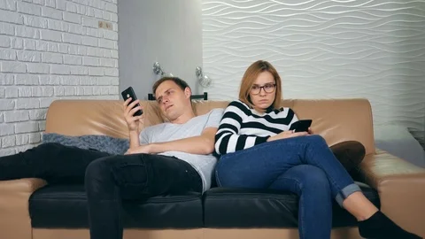 Attractive young couple sitting back to back at home on couch obsessed with s Stock Footage 121502732