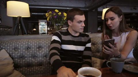 Attractive young couple talking and using smartphone at cafe Stock Footage 68999060