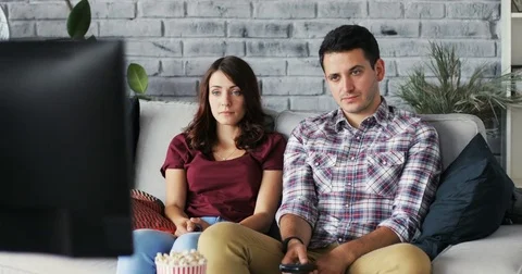 Attractive young couple watching tv on couch at home boring girl channel Stock Footage