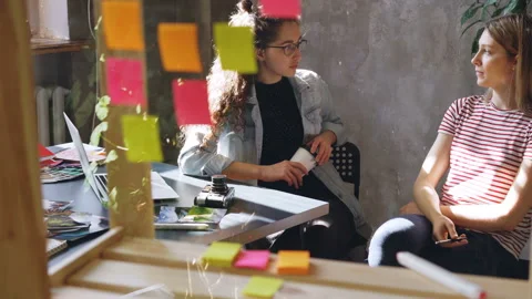 An attractive young designer is talking to her colleague in workplace. Women are Stock Footage