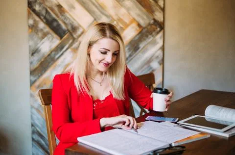 Attractive young girl in a red jacket works at a table with papers and device Stock Photos