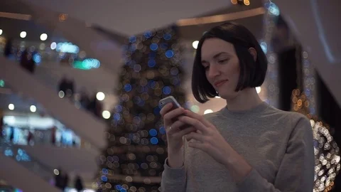 Attractive young girl smiling using smartphone in a crowded shopping mall Stock Footage 83367402
