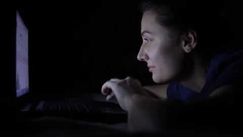 An attractive young girl is using a mobile computer while lying on a bed at Stock Footage 100721509