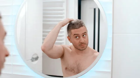 Attractive young guy applying moisturiser cream on eyebrows looking in mirror Video stock 254069656