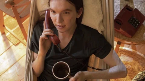 An attractive young guy with long hair is lying in a suspended hammock Stock Footage 245992053