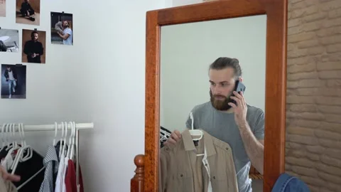 Attractive young guy is looking into the mirror / Talking calling on phone Stock Footage 147893926