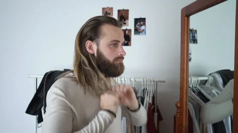 Attractive young guy is looking into the mirror combing hair Stock Footage 147899529
