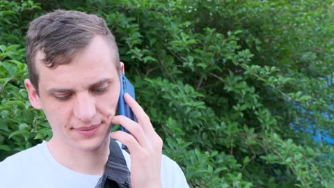Attractive Young guy talking on the phone on green bushes background Video stock 134392642