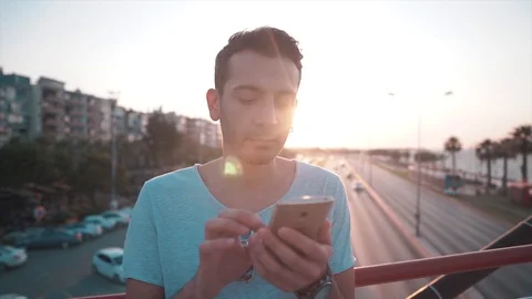 Attractive young handsome man is tapping mobile phone on bridge with sunlight.  Stock Footage 112894585