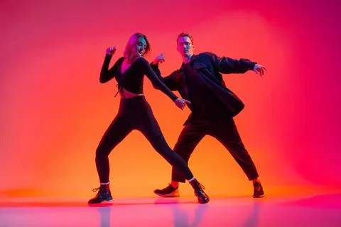 Attractive young man and woman dancing hip-hop isolated on gradient pink studio Stock Photos