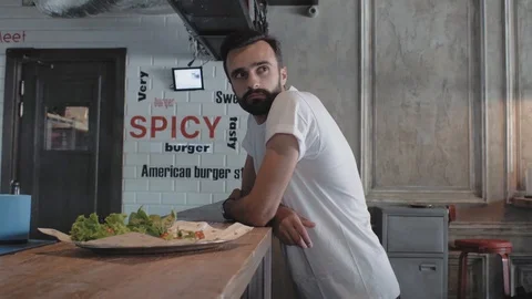 Attractive young man with a beard stands near the bar, waiting for his burger Stock Footage 115634057