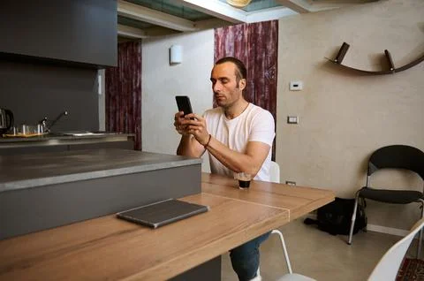 Attractive young man checking mobile app on his smartphone, sitting at table  스톡 사진